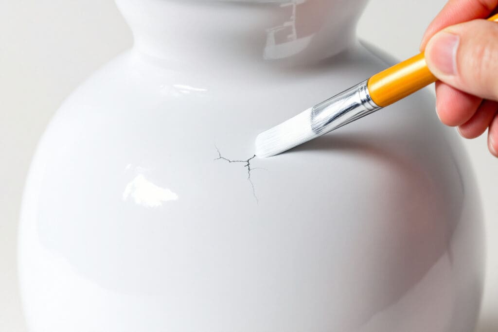 a symbolic photo showing signs your ex is pretending depicting a hand painting over a crack in a vase with the imperfection still subtly visible